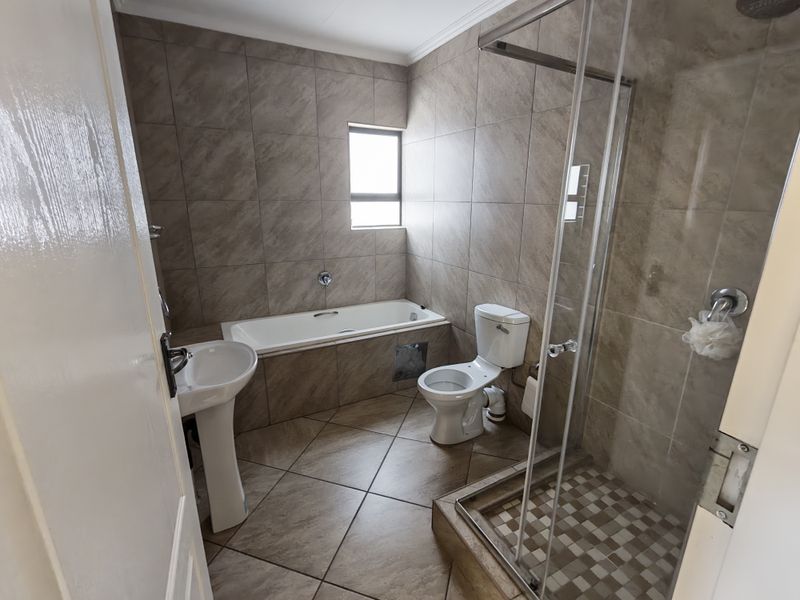 A functional bathroom featuring a pedestal basin, built-in bathtub, toilet, and a separate glass-enclosed shower with neutral floor-to-ceiling tiling.