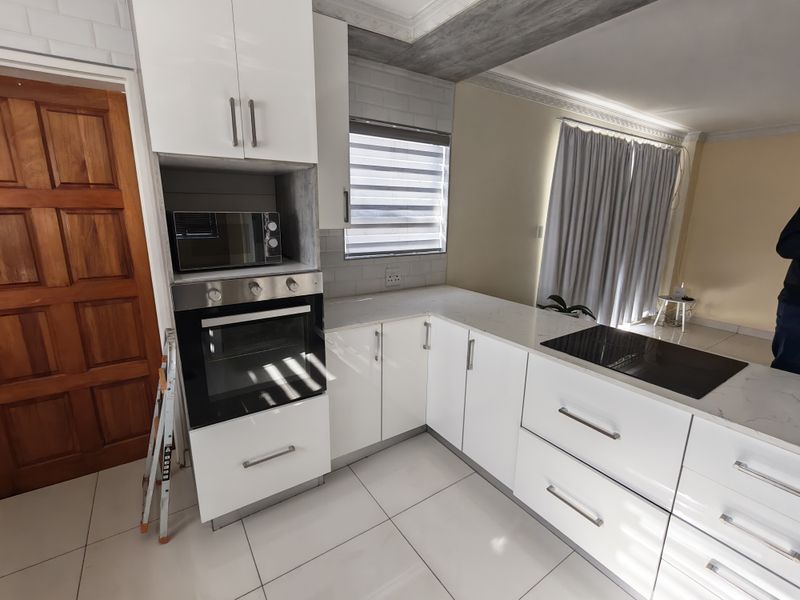 Modern kitchen featuring white cabinetry, stone countertops, built-in oven, electric cooktop, and tiled flooring with a clean, contemporary finish.
