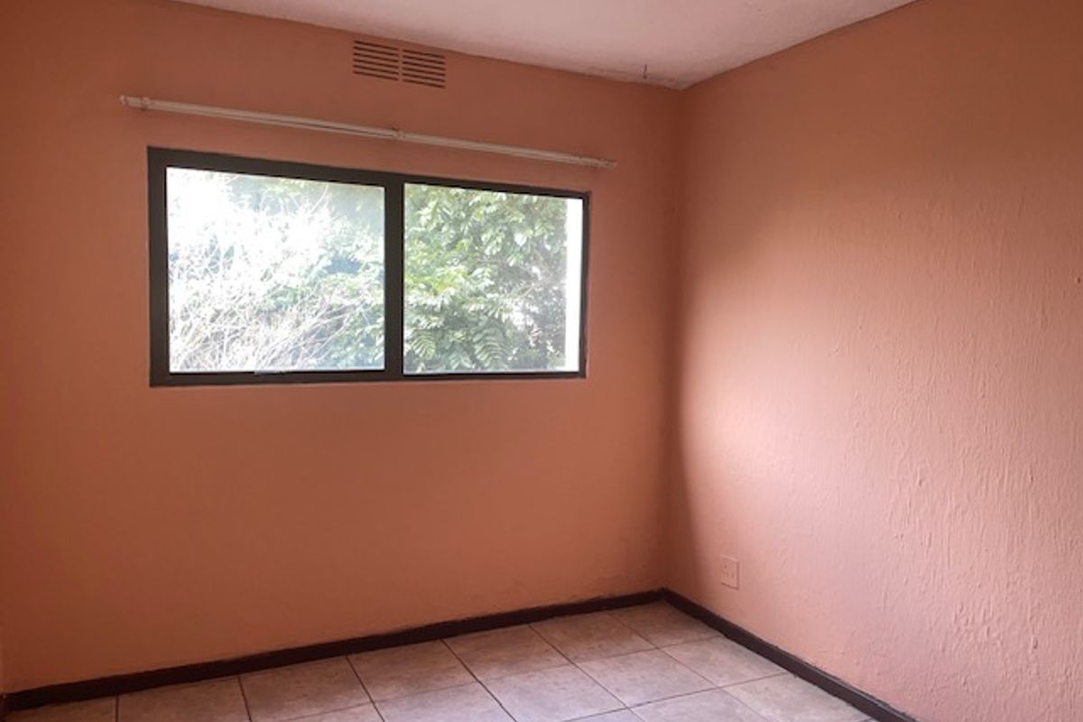 An empty bedroom featuring tiled flooring, a window with a curtain rod, and a ventilation grille, ready for renovation or staging.