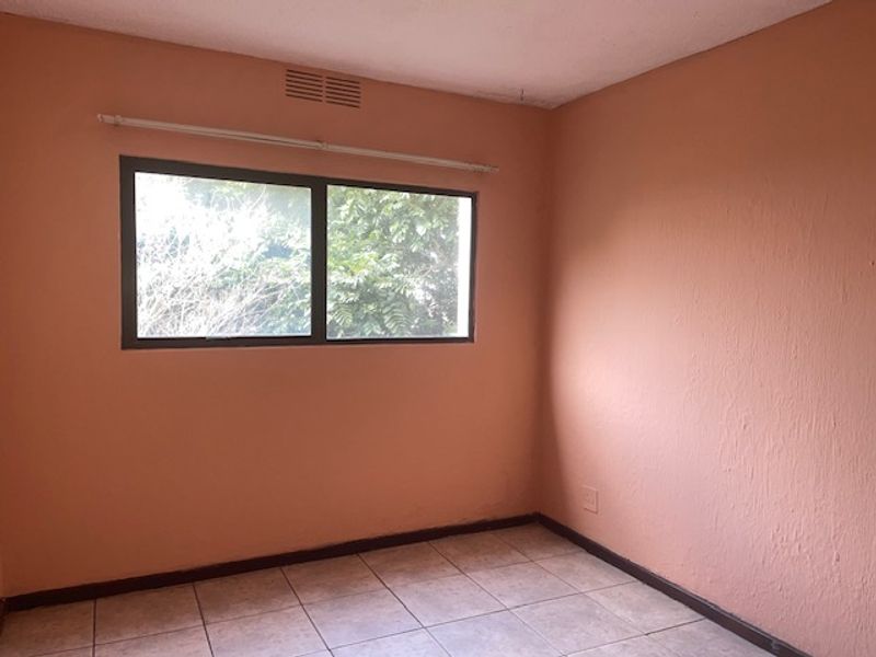 An empty bedroom featuring tiled flooring, a window with a curtain rod, and a ventilation grille, ready for renovation or staging.