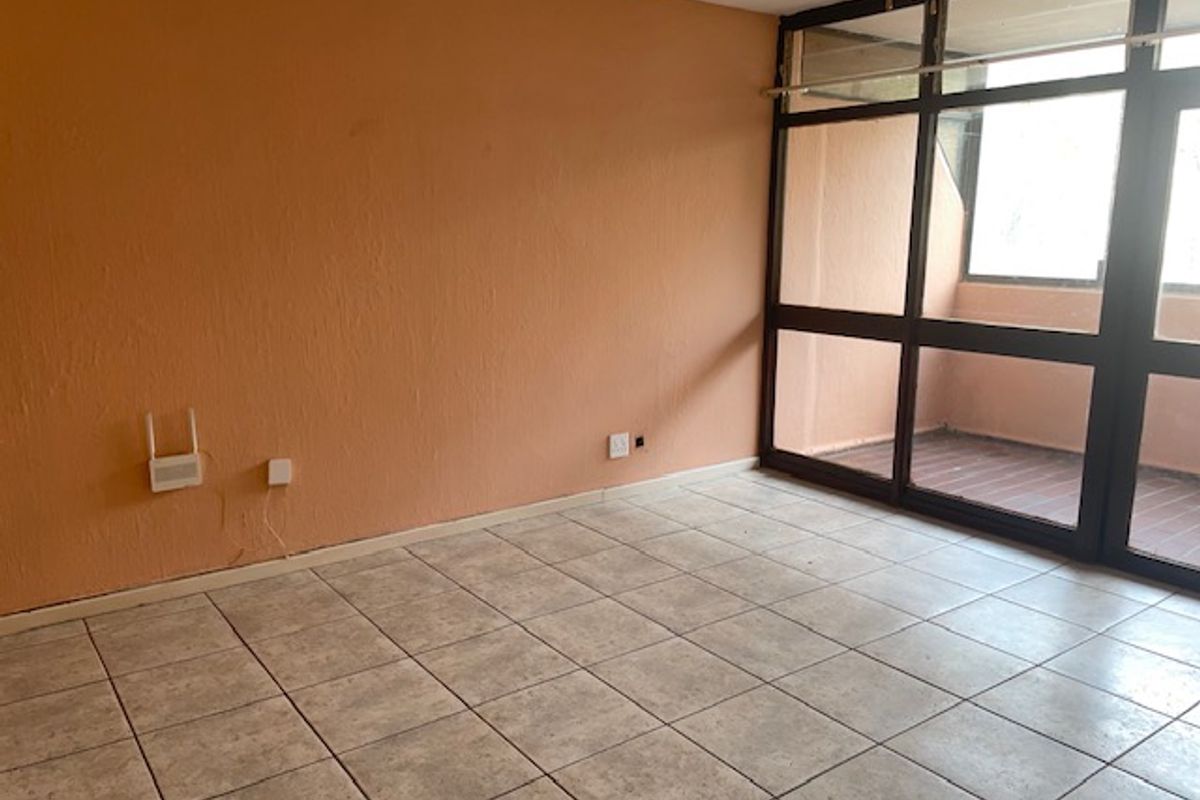 An empty living room featuring tiled flooring and large glass sliding doors leading to an outdoor area, requiring cosmetic updates to the walls.