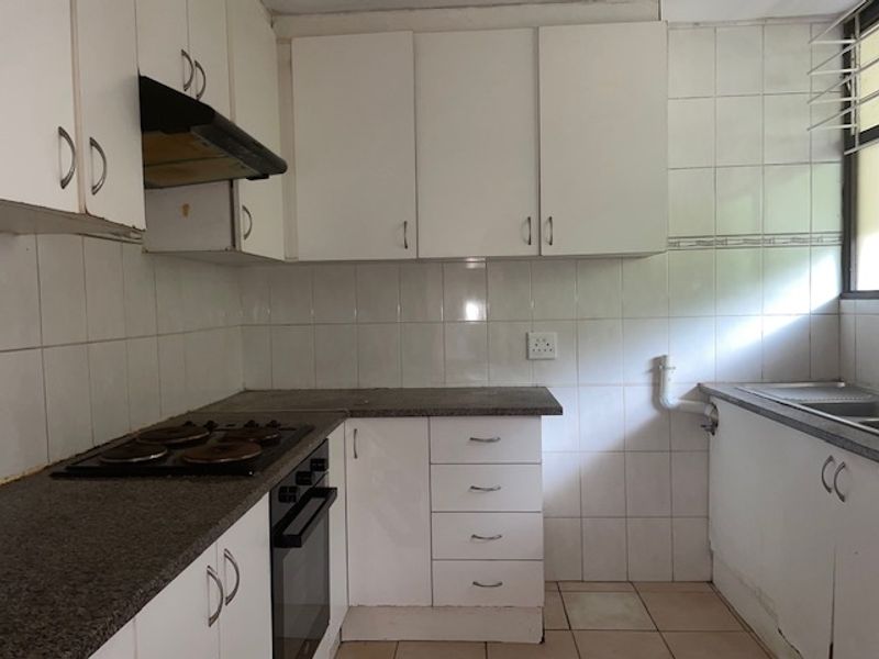A functional kitchen featuring white cabinetry, laminate countertops, an integrated electric hob, oven, and tiled splashbacks, offering a blank canvas for modernization.