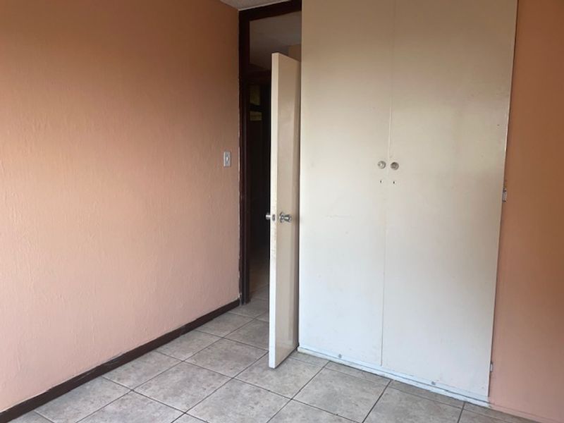 An empty bedroom featuring tiled flooring and a built-in wardrobe, ready for renovation or staging.