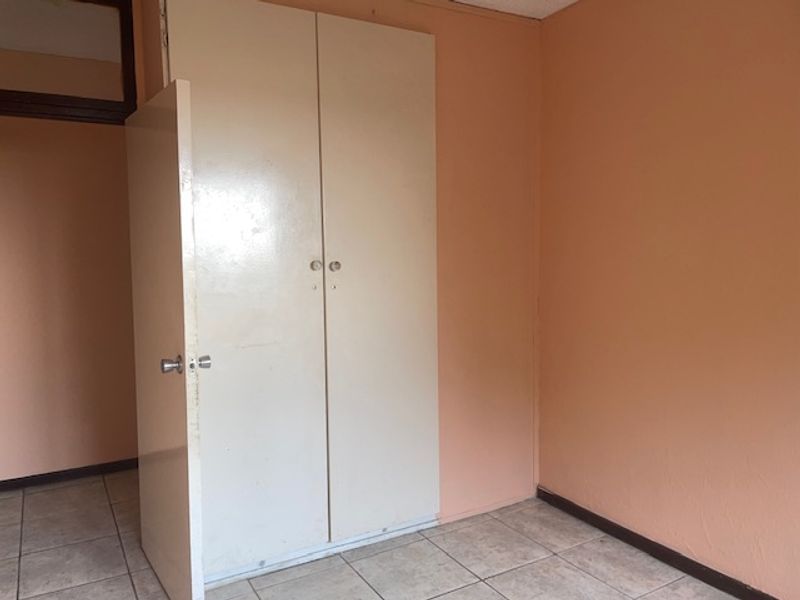 An empty bedroom featuring tiled flooring and a built-in cupboard, presenting a blank canvas for potential renovation or restyling.