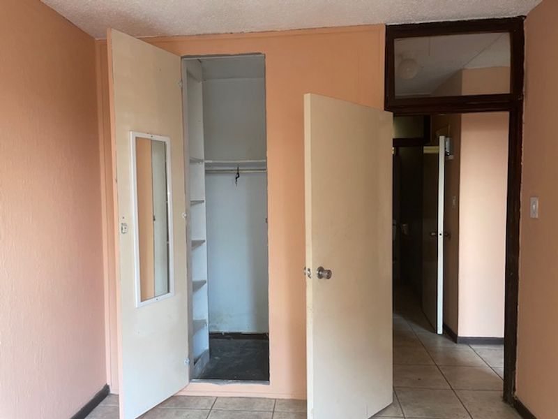 An empty bedroom featuring tiled flooring, a built-in closet with shelving, and a transom window above the doorway, awaiting cosmetic updates.