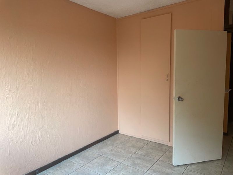 An empty bedroom featuring tiled flooring and a built-in cupboard, offering a blank canvas for personalization.