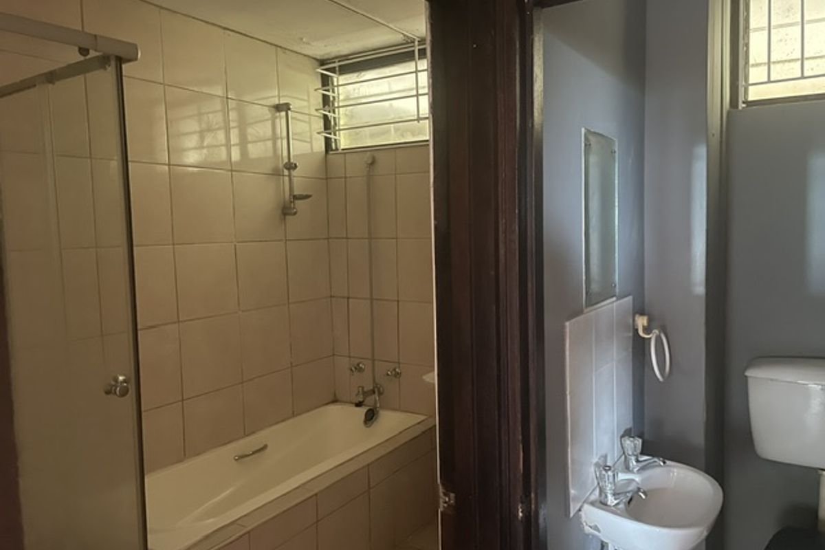 A dated bathroom featuring a bathtub with shower mixer, a wall-mounted basin, and a toilet, requiring cosmetic updates to improve its overall condition.