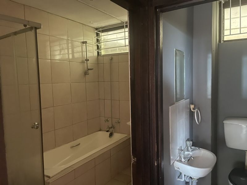 A dated bathroom featuring a bathtub with shower mixer, a wall-mounted basin, and a toilet, requiring cosmetic updates to improve its overall condition.