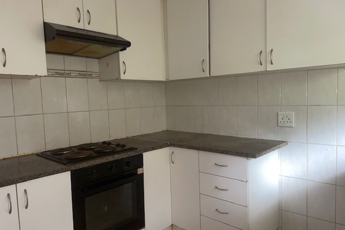 A compact kitchen featuring white built-in cabinetry, laminate countertops, an integrated electric oven and hob, and a tiled splashback.