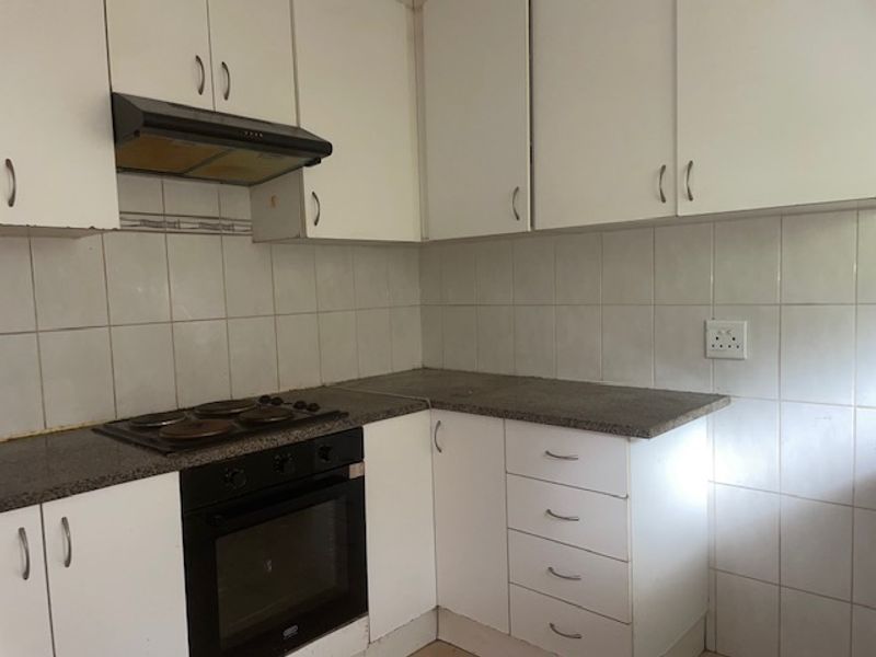 A compact kitchen featuring white built-in cabinetry, laminate countertops, an integrated electric oven and hob, and a tiled splashback.