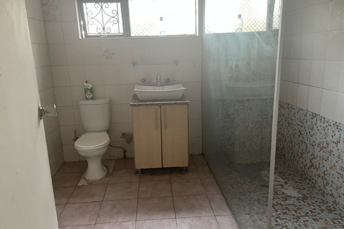 A functional bathroom featuring a vessel sink vanity, a toilet, and a walk-in shower with glass screen and mosaic tile detailing.