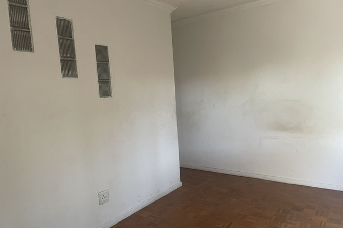 An empty living room featuring original parquet flooring and decorative glass block wall inserts, requiring cosmetic updates to the wall finishes.