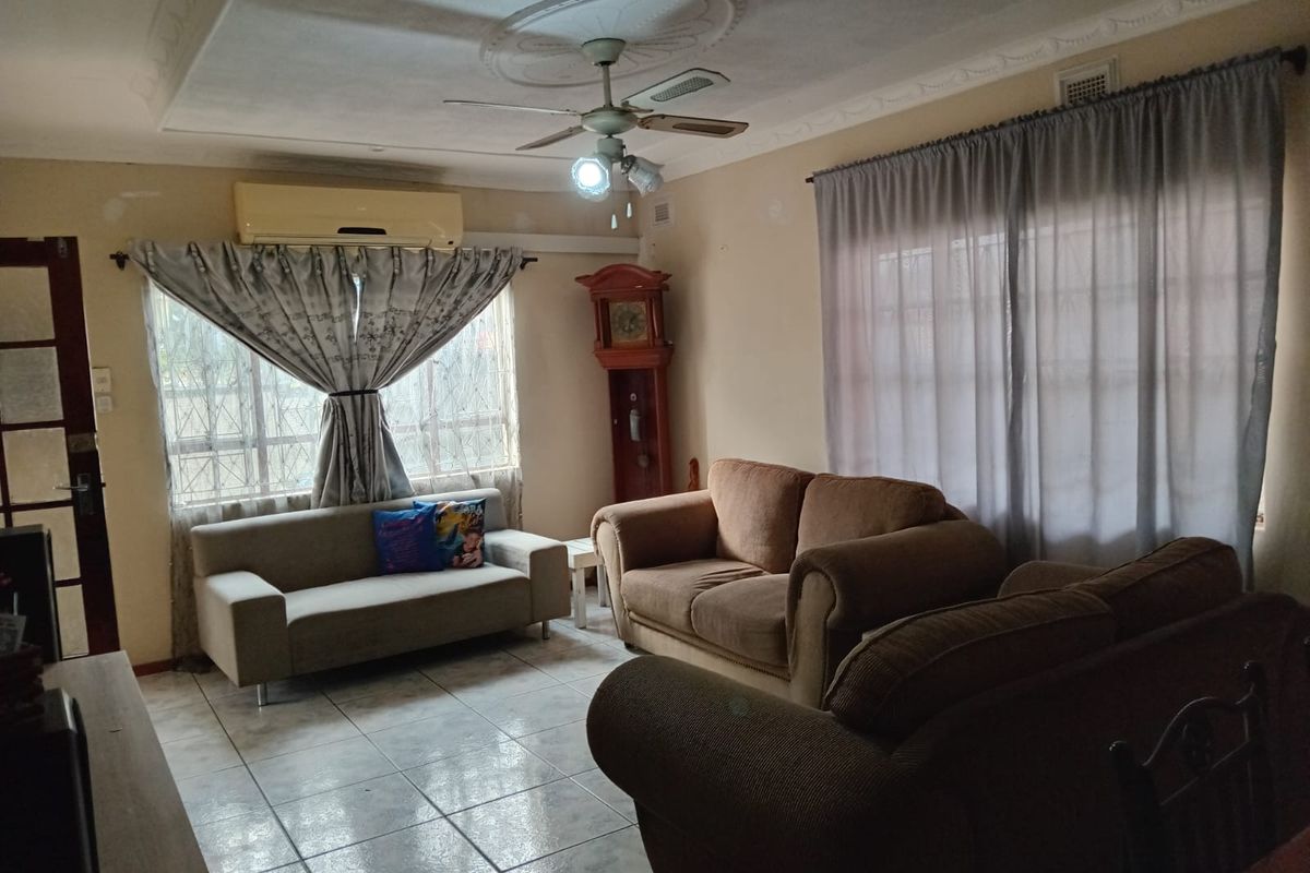 A living room featuring ceramic tiled flooring, a ceiling fan with decorative rose, and a wall-mounted air conditioning unit.