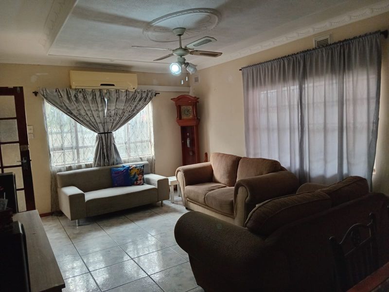 A living room featuring ceramic tiled flooring, a ceiling fan with decorative rose, and a wall-mounted air conditioning unit.