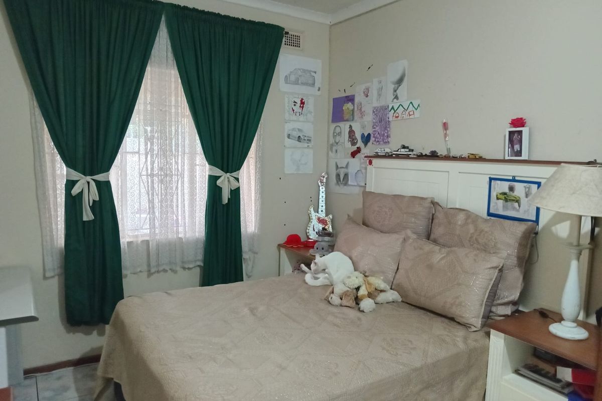 A functional bedroom featuring a built-in headboard, tiled flooring, and a window fitted with security bars.
