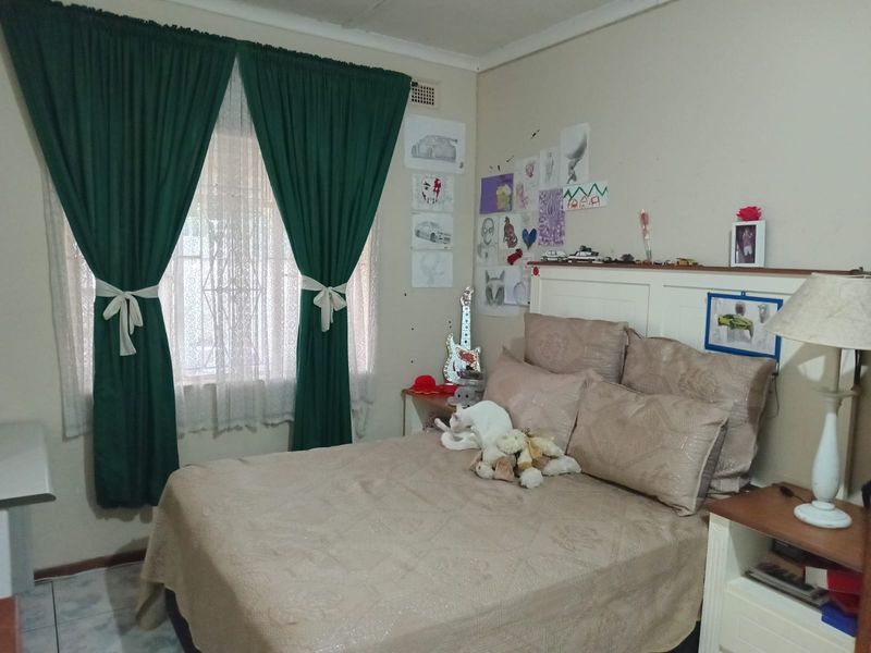 A functional bedroom featuring a built-in headboard, tiled flooring, and a window fitted with security bars.