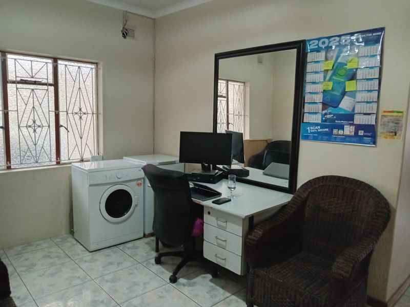 A functional utility space featuring tiled flooring, security window bars, and a large wall-mounted mirror, currently utilized as a home office and laundry area.