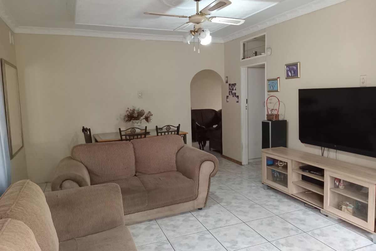 A living room featuring ceramic floor tiles, a ceiling fan with decorative rose, and coved cornicing, leading through an arched doorway to another space.