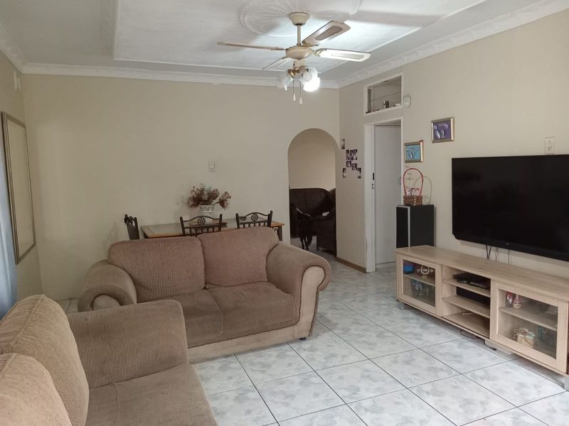 A living room featuring ceramic floor tiles, a ceiling fan with decorative rose, and coved cornicing, leading through an arched doorway to another space.