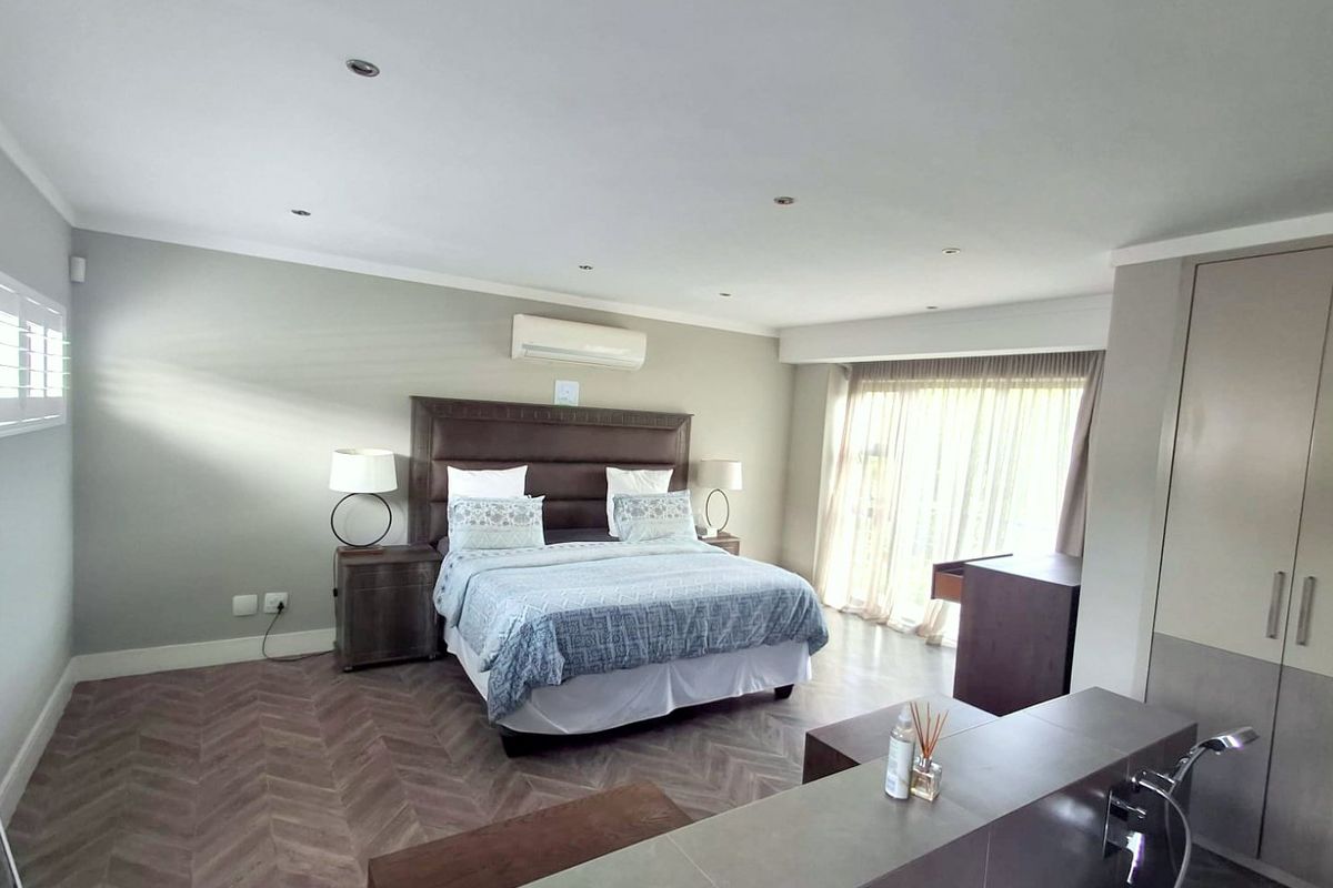 Spacious bedroom featuring herringbone flooring, recessed lighting, a split-system air conditioner, and built-in cupboards with access to a patio through sliding glass doors.