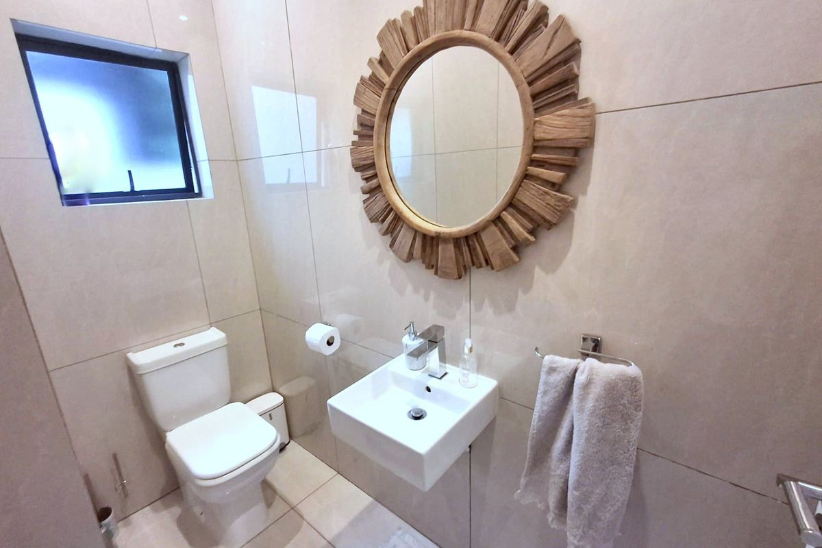 A modern guest bathroom featuring neutral wall-to-wall tiling, a wall-mounted basin with a mixer tap, and a sleek top-flush toilet.
