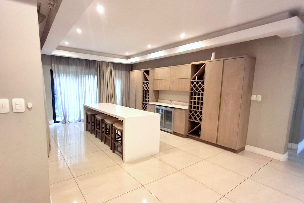 Modern kitchen featuring light wood cabinetry, a large central island with seating, integrated wine storage, and sleek tiled flooring.