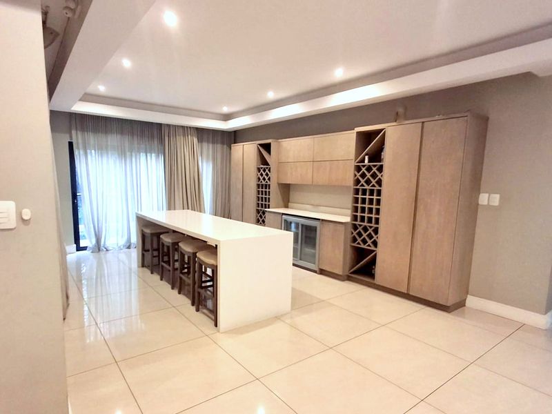 Modern kitchen featuring light wood cabinetry, a central island with seating, integrated wine storage, and polished tile flooring under recessed lighting.