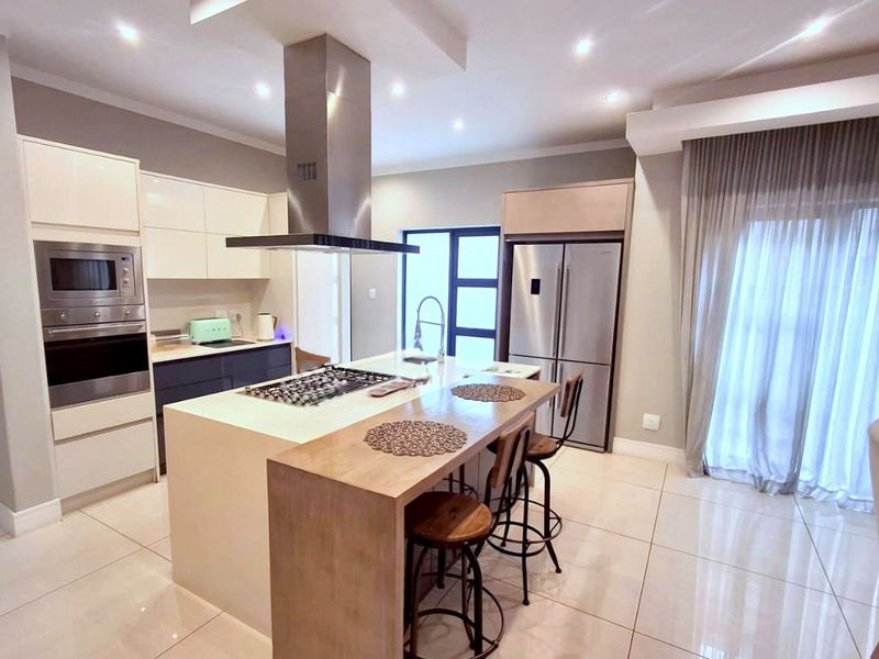 Modern kitchen featuring a central island with a gas hob, built-in oven and microwave, sleek cabinetry, and polished tiled flooring.