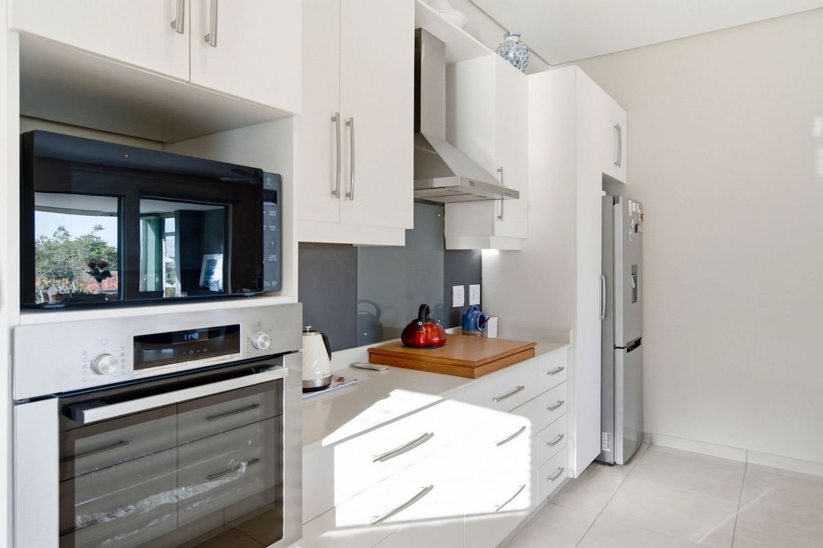 Modern kitchen featuring white cabinetry, stone countertops, glass splashback, and integrated stainless steel appliances including an oven, microwave, and extractor fan.