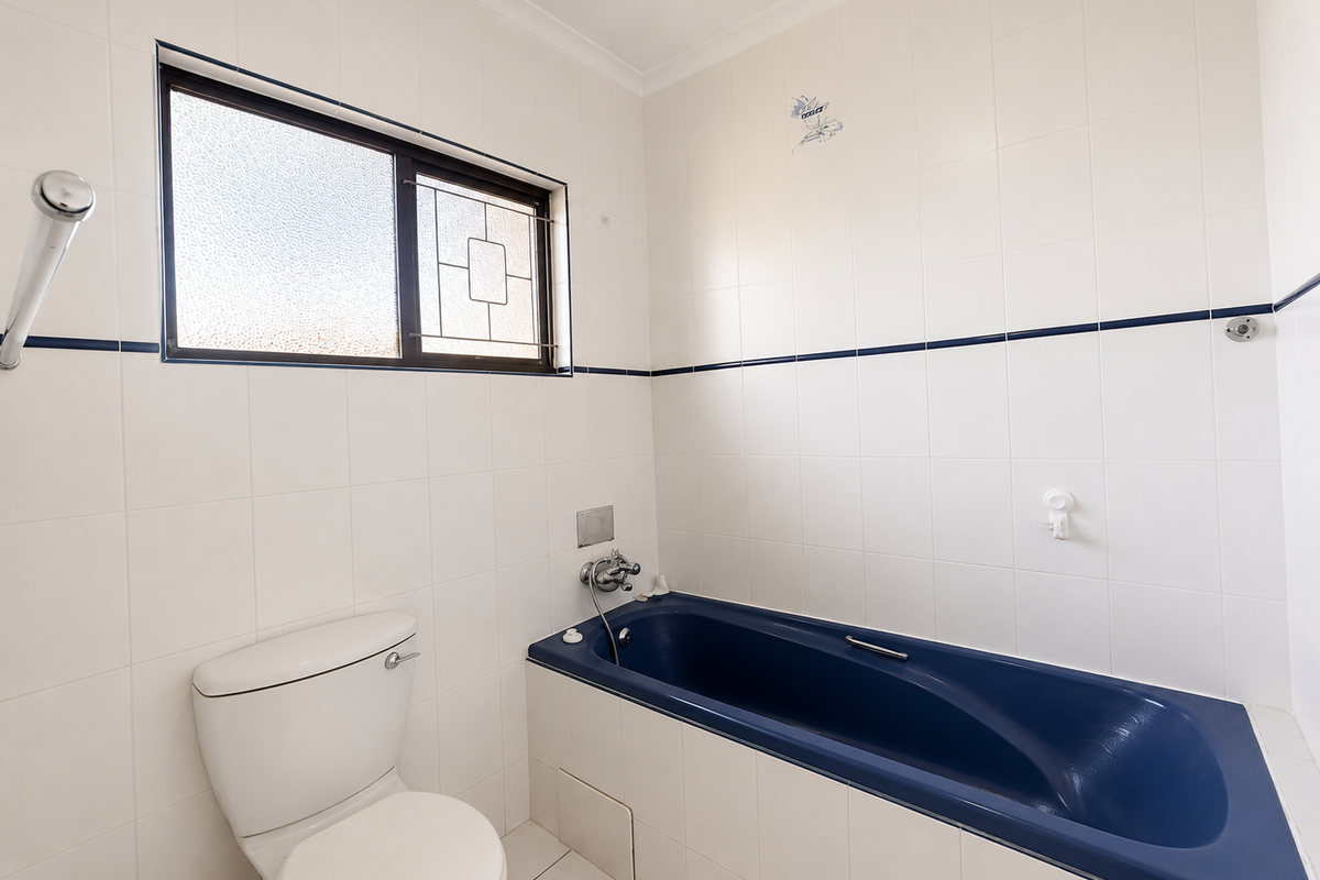 A functional bathroom featuring white wall tiles with a blue accent border, a blue built-in bathtub, and a standard toilet.