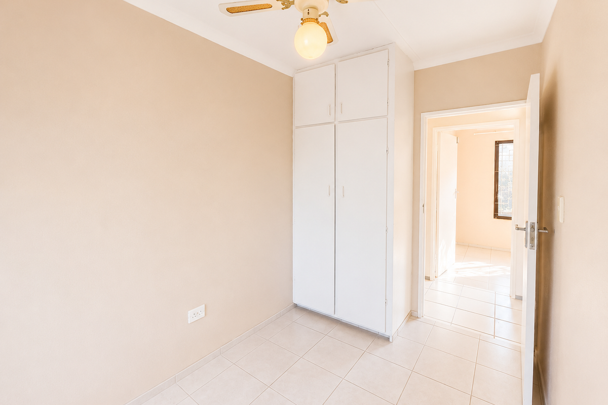 An empty bedroom featuring neutral walls, tiled flooring, a built-in wardrobe, and a ceiling fan, with an open doorway leading to an adjacent room.