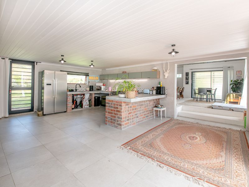 Spacious open-plan kitchen and living area featuring exposed brick elements, concrete countertops, and large format floor tiles with direct access to the outdoors.
