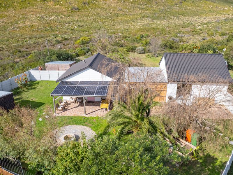 Aerial view of a residential property featuring a metal roof, solar panel installation, covered patio, and a landscaped garden with a stone fire pit.