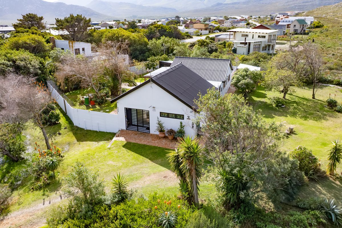 Aerial view of a detached house featuring a corrugated metal roof, brick patio, and expansive surrounding garden in a quiet residential setting.