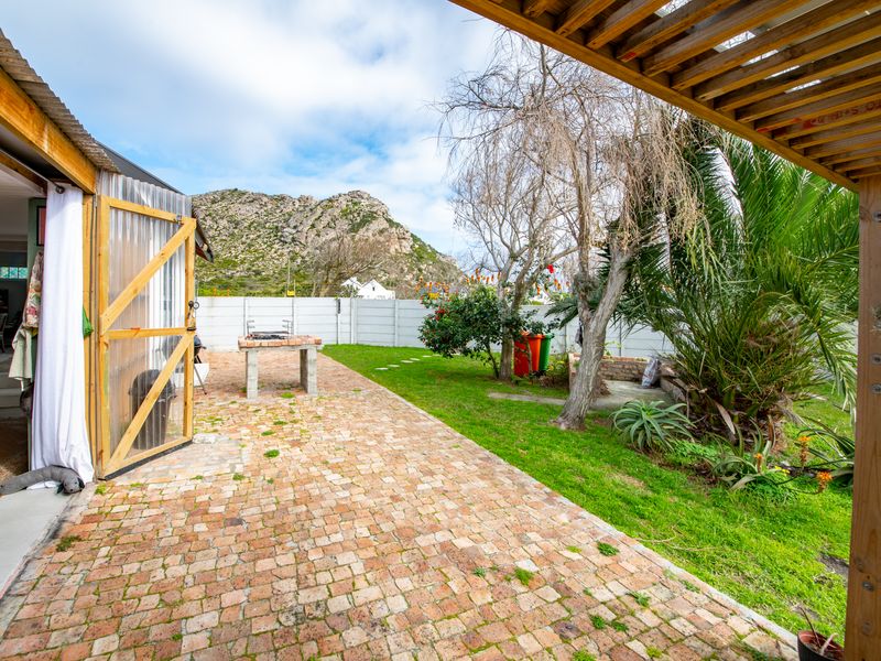 Outdoor patio area featuring brick paving, a timber pergola, and a built-in brick braai, set within a garden with mountain views.