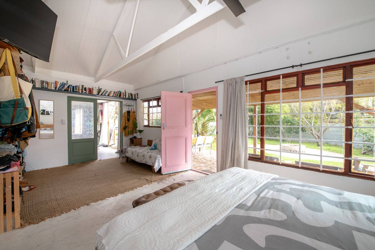 Spacious bedroom featuring vaulted ceilings with exposed trusses, large timber-framed windows, and direct access to the garden area.