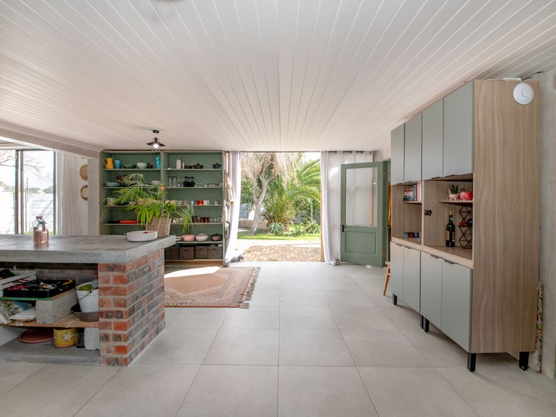 Spacious open-plan living area featuring a unique exposed brick kitchen island with concrete countertop, built-in cabinetry, and direct access to the garden.