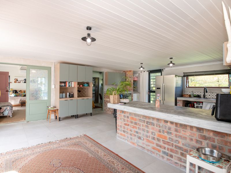 Spacious open-plan kitchen and living area featuring an exposed brick island with concrete countertop, tiled floors, and a distinctive tongue and groove ceiling.