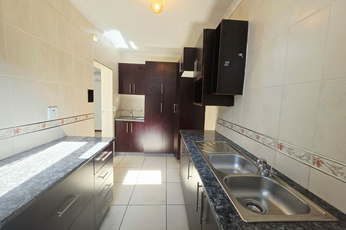 A functional galley-style kitchen featuring dark wood cabinetry, laminate countertops, and a double stainless steel sink with tiled walls and flooring.