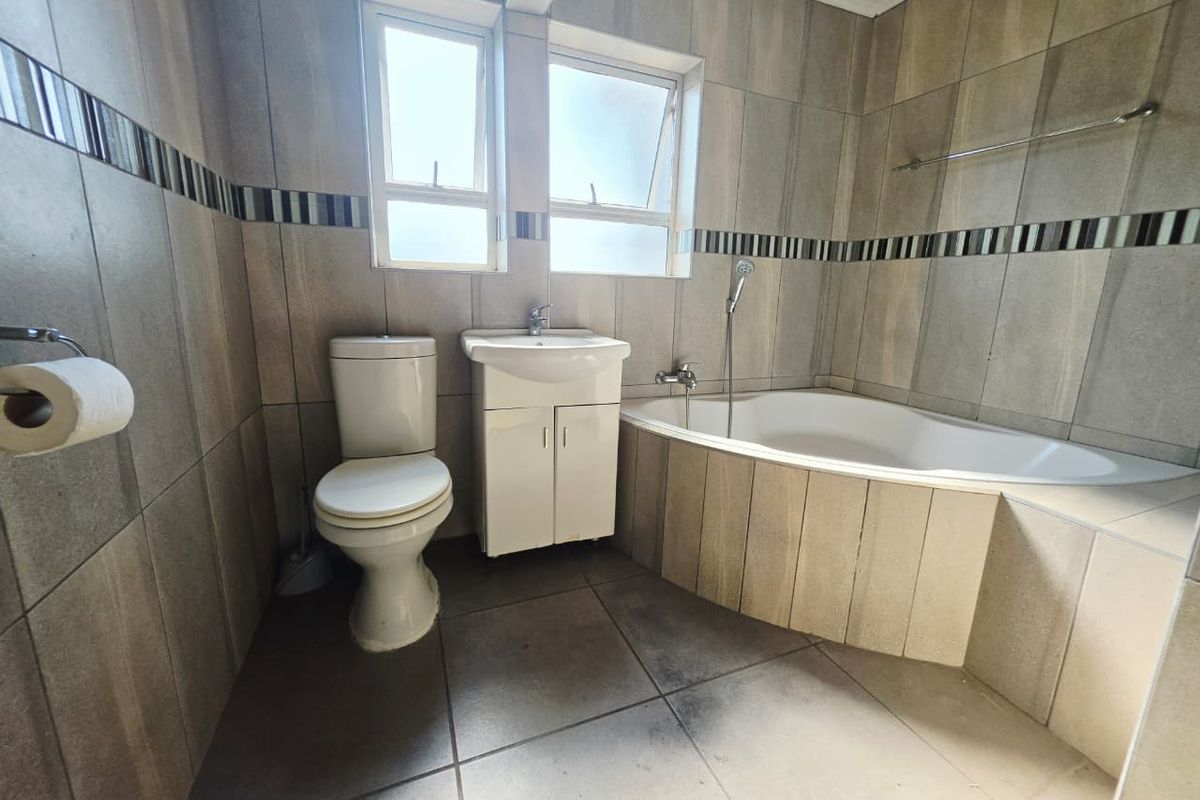 A functional bathroom featuring a corner bathtub, vanity basin, and toilet with neutral wall and floor tiling.