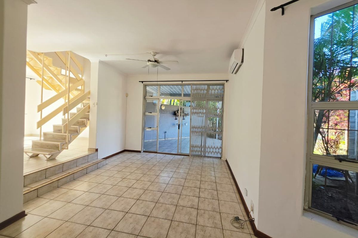 Spacious, light-filled living area featuring tiled flooring, a staircase, and direct access to an outdoor patio through sliding glass doors.