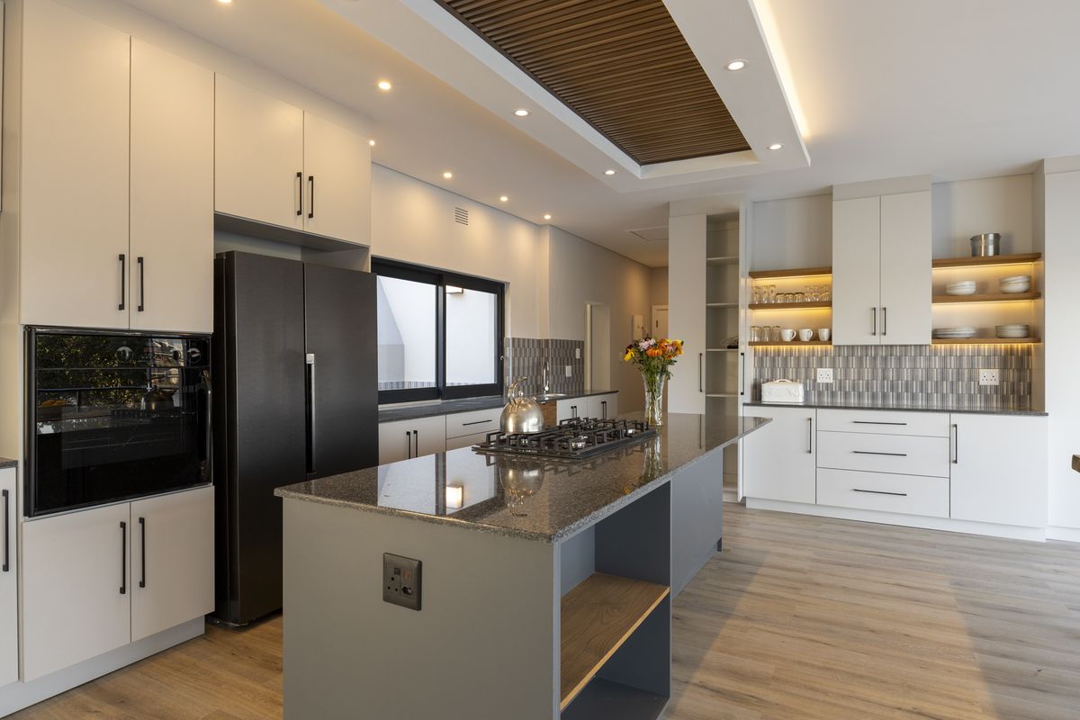 Modern kitchen featuring a central island with gas cooktop, granite countertops, sleek cabinetry, and a decorative timber slat ceiling detail with recessed lighting.