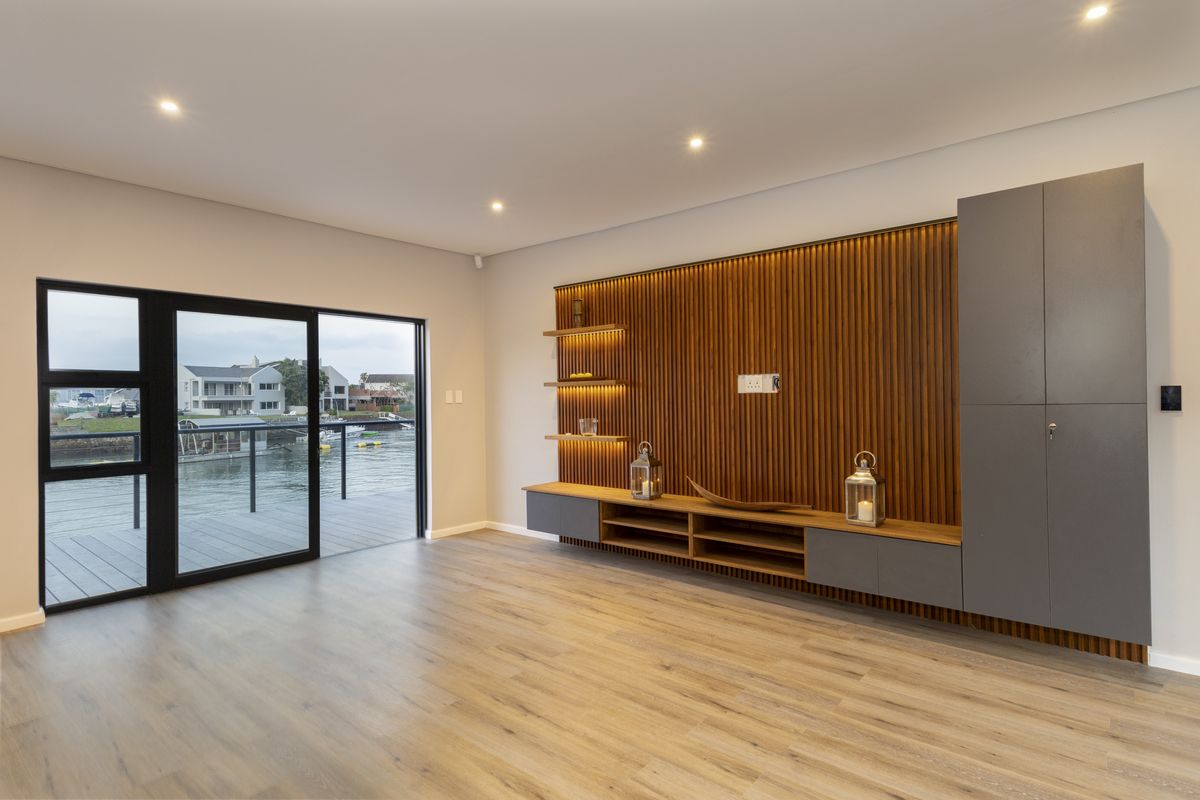 Modern living room featuring a timber slat feature wall, built-in cabinetry, laminate flooring, and a sliding glass door with water views.