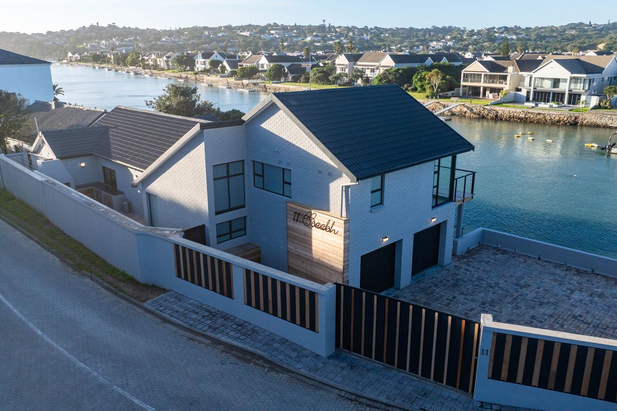 Aerial view of a modern waterfront house featuring a tiled roof, brick and timber facade, double garage, and secure perimeter walling.