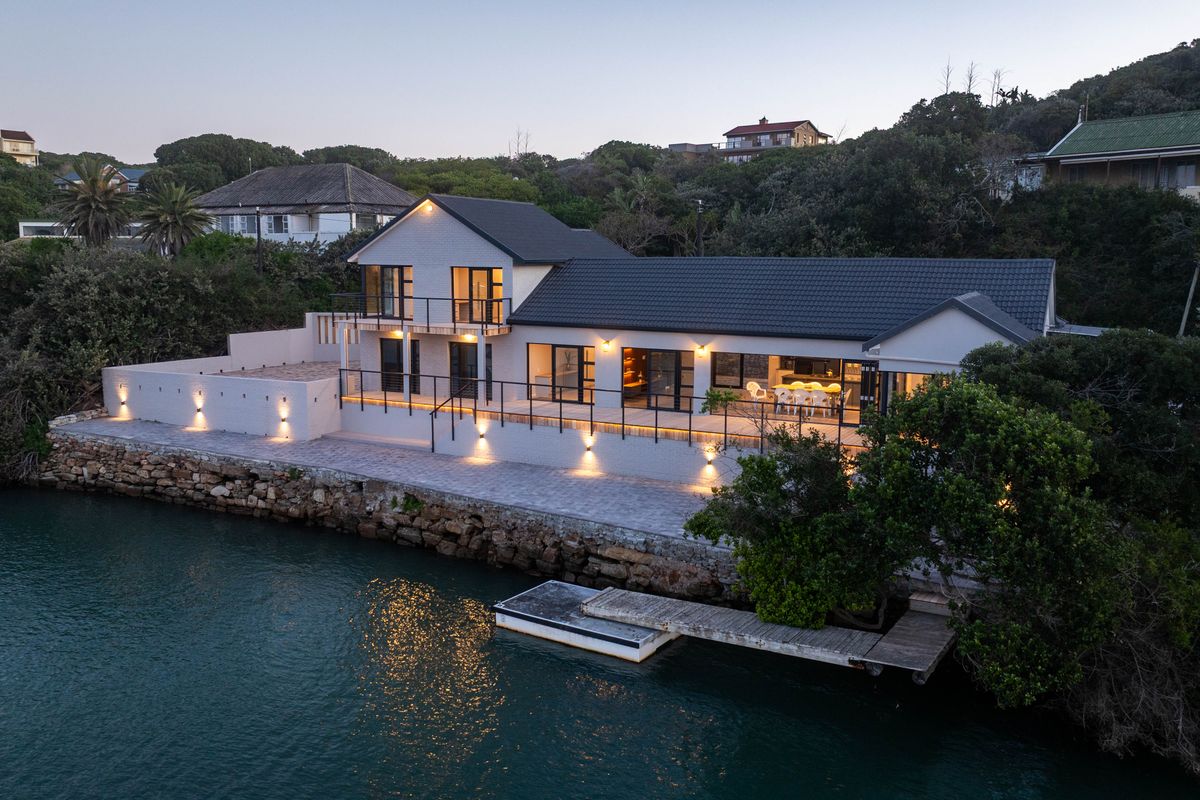 Stunning waterfront property featuring a spacious paved patio, private jetty, and modern architectural design with integrated exterior lighting.