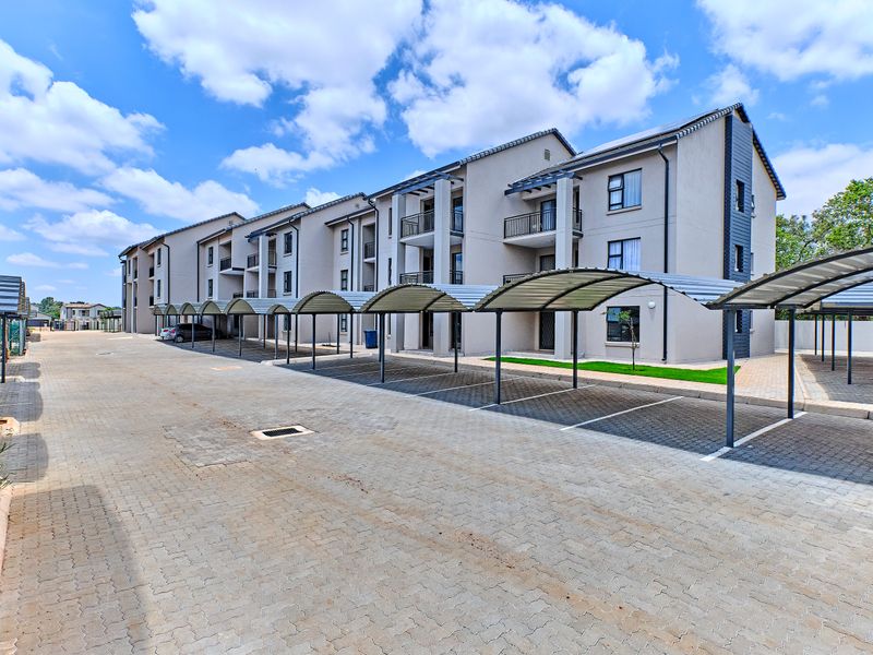 Exterior view of a modern apartment complex featuring paved parking areas with covered bays and private balconies for residents.