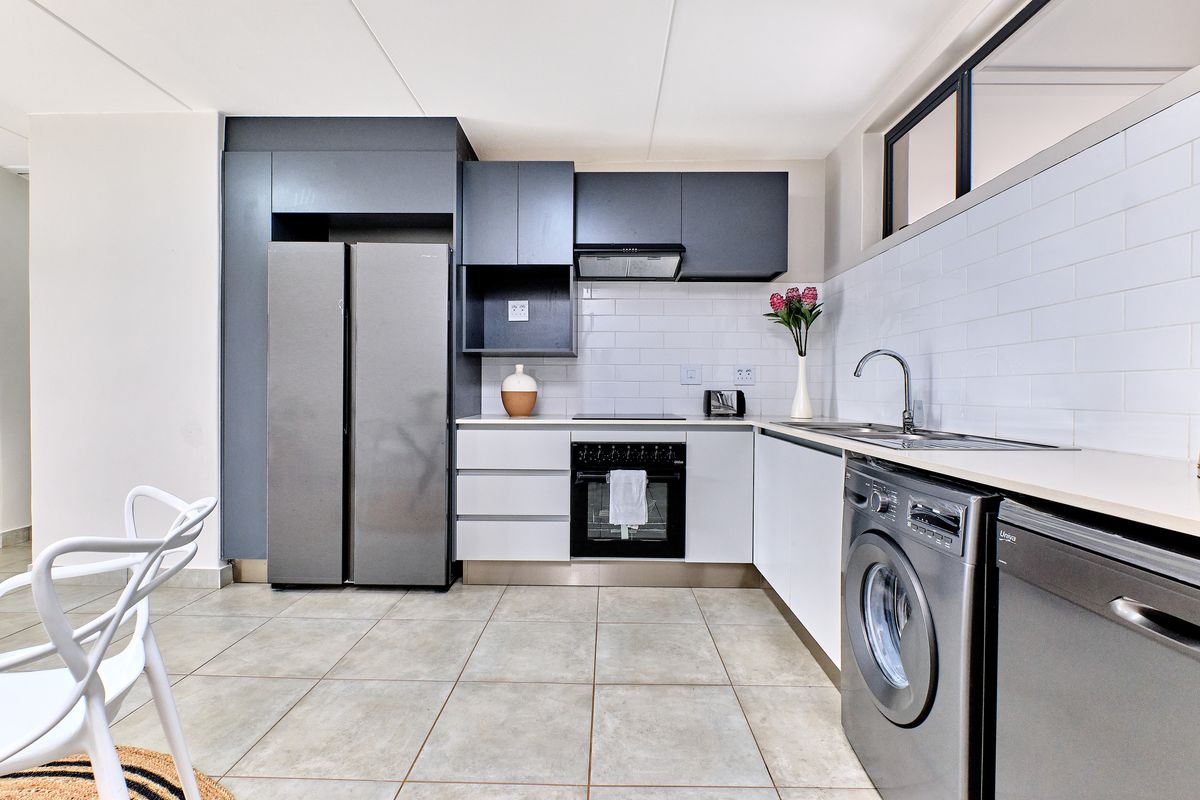 Modern kitchen featuring dark grey cabinetry, white subway tile backsplash, integrated appliances, and neutral ceramic floor tiles.