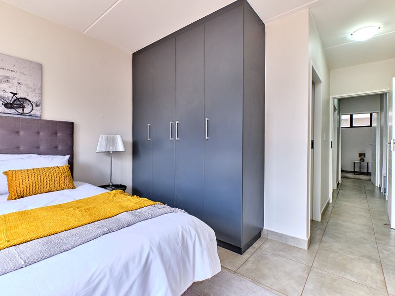 A well-maintained bedroom featuring a modern dark grey built-in wardrobe, neutral tiled flooring, and direct access to an adjacent hallway.