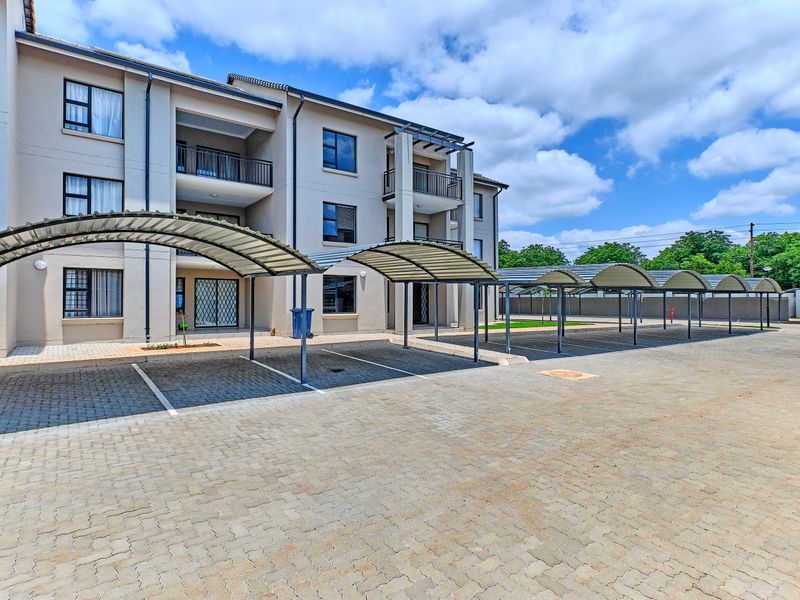 Exterior view of a modern apartment complex featuring multiple covered parking bays and paved driveway access.