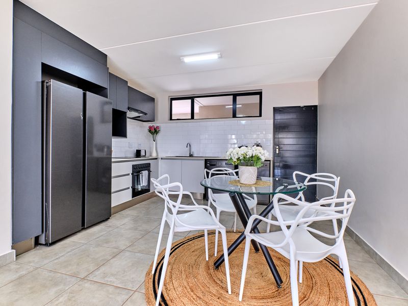 Modern open-plan kitchen featuring sleek dark cabinetry, subway tile backsplash, and tiled flooring, seamlessly integrated with a dining area.